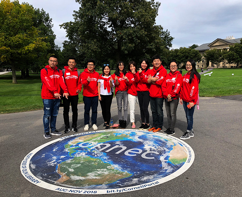 Cornell students posing by a sign on the Arts Quad