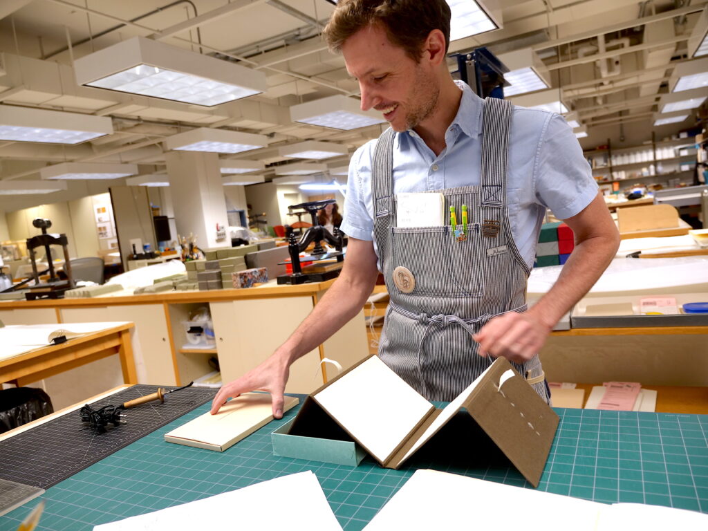 A conservator at his work desk with a model of a book enclosure he's designing